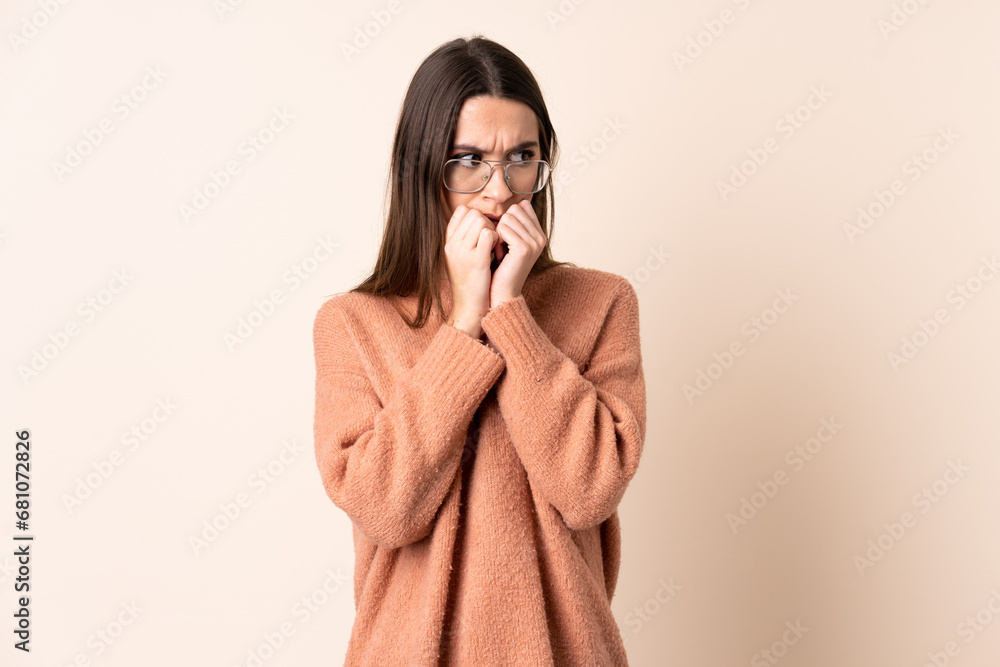 Young woman over isolated beige background nervous and scared putting hands to mouth Young woman over isolated beige background nervous and scared putting hands to mouth