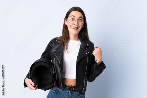 Young woman holding a motorcycle helmet over isolated blue background celebrating a victory © luismolinero