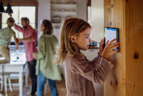 Girl looking at smart thermostat at home, checking heating temperature. Concept of sustainable, efficient, and smart technology in home heating and thermostats. photo