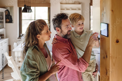 Family looking at smart thermostat, adjusting, lowering heating temperature at home. Concept of sustainable, efficient, and smart technology in home heating and thermostats. photo