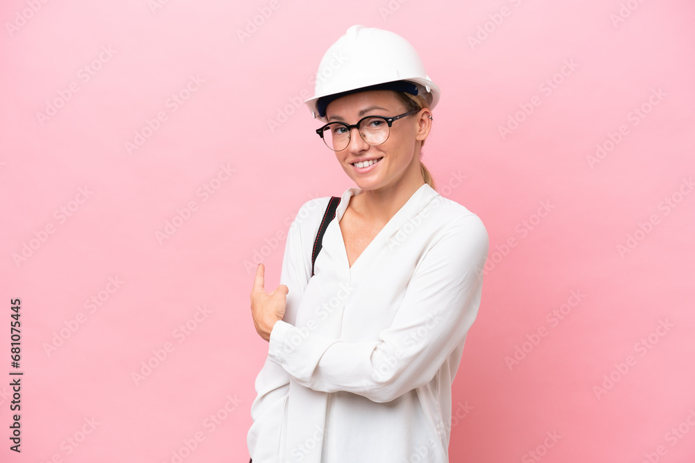 Young architect Russian woman with helmet and holding blueprints isolated on pink background pointing back Young architect Russian woman with helmet and holding blueprints isolated on pink background pointing back