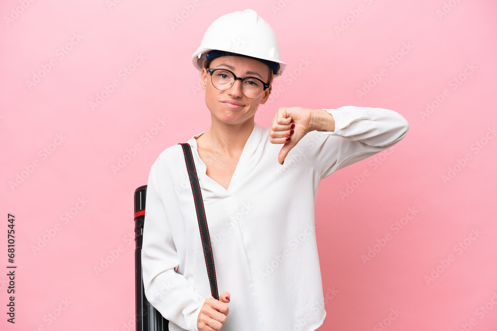 Young architect Russian woman with helmet and holding blueprints isolated on pink background showing thumb down with negative expression Young architect Russian woman with helmet and holding blueprints isolated on pink background showing thumb down with negative expression