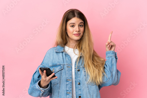 Young blonde woman isolated on blue background using mobile phone and lifting finger