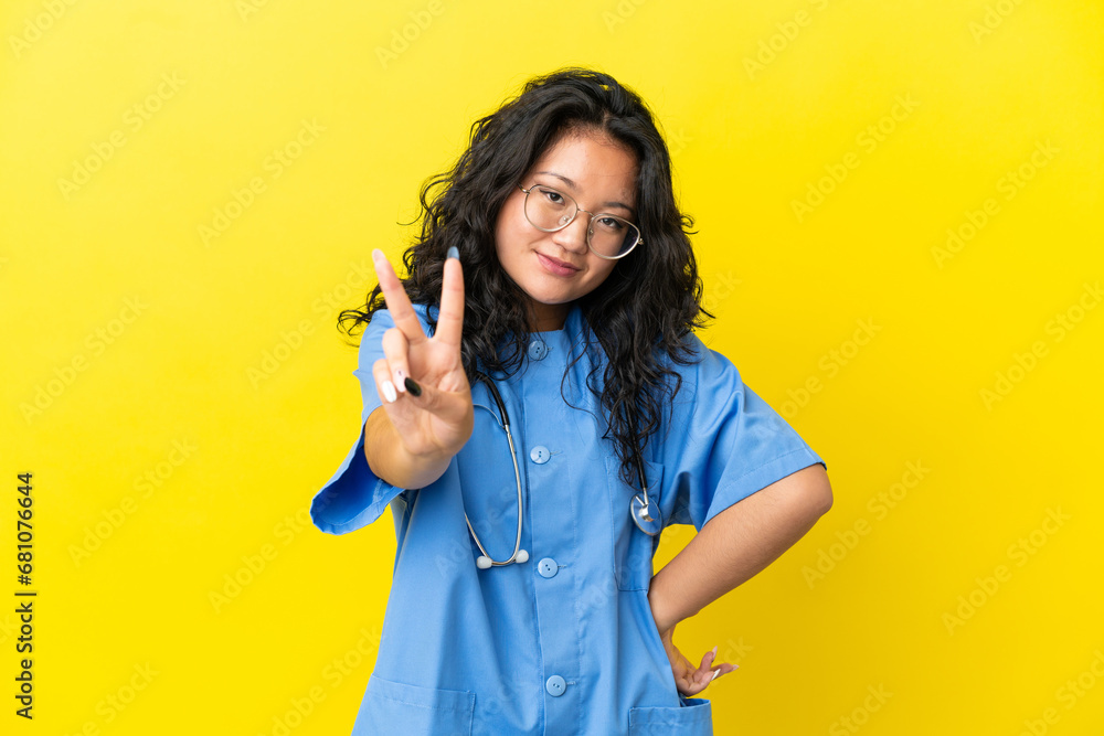 Young surgeon doctor asian woman isolated on yellow background smiling and showing victory sign Young surgeon doctor asian woman isolated on yellow background smiling and showing victory sign