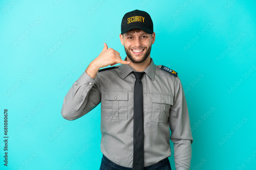 Young security man isolated on blue background making phone gesture. Call me back sign Young security man isolated on blue background making phone gesture. Call me back sign