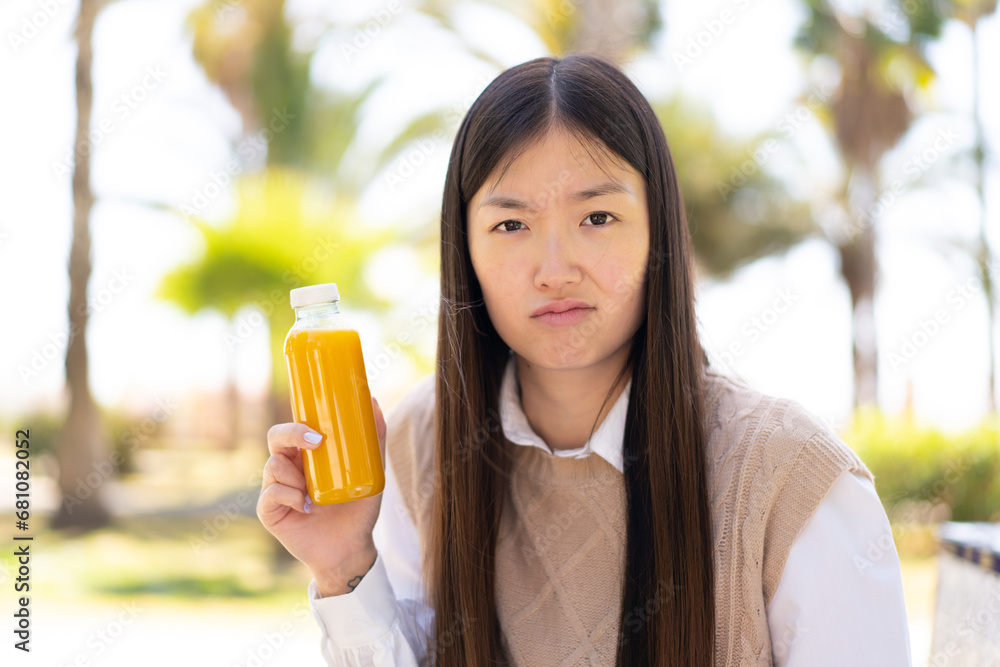 Pretty Chinese woman holding an orange juice at outdoors with sad expression Pretty Chinese woman holding an orange juice at outdoors with sad expression