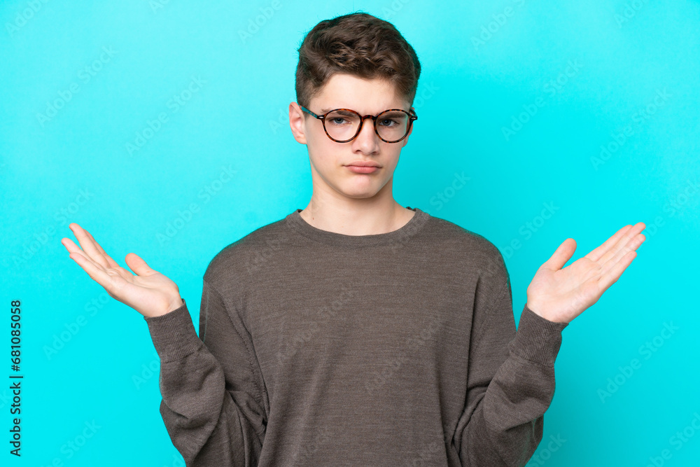 Teenager Russian man isolated on blue background making doubts gesture Teenager Russian man isolated on blue background making doubts gesture