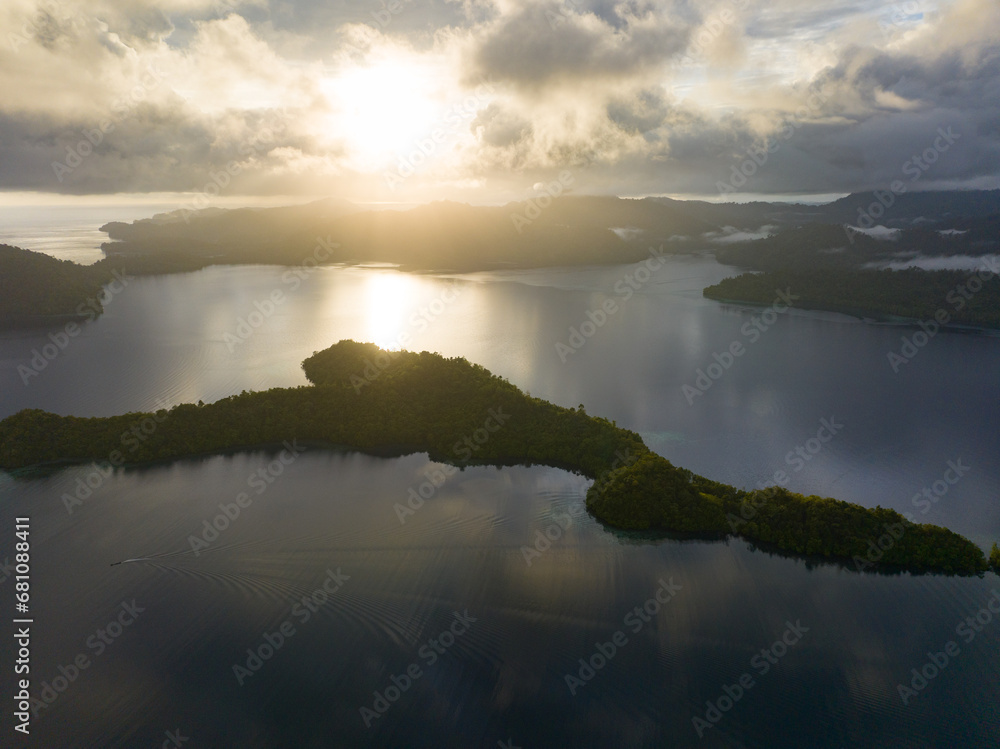 Fototapeta premium Low, sunlit clouds drift across the island of Batanta in Raja Ampat, Indonesia, at dawn. This area is known as the heart of the Coral Triangle due to its incredibly high marine biodiversity.
