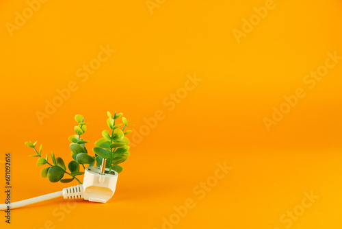 Fototapeta Naklejka Na Ścianę i Meble -  Green plant with electric plug on orange background with copy space for text