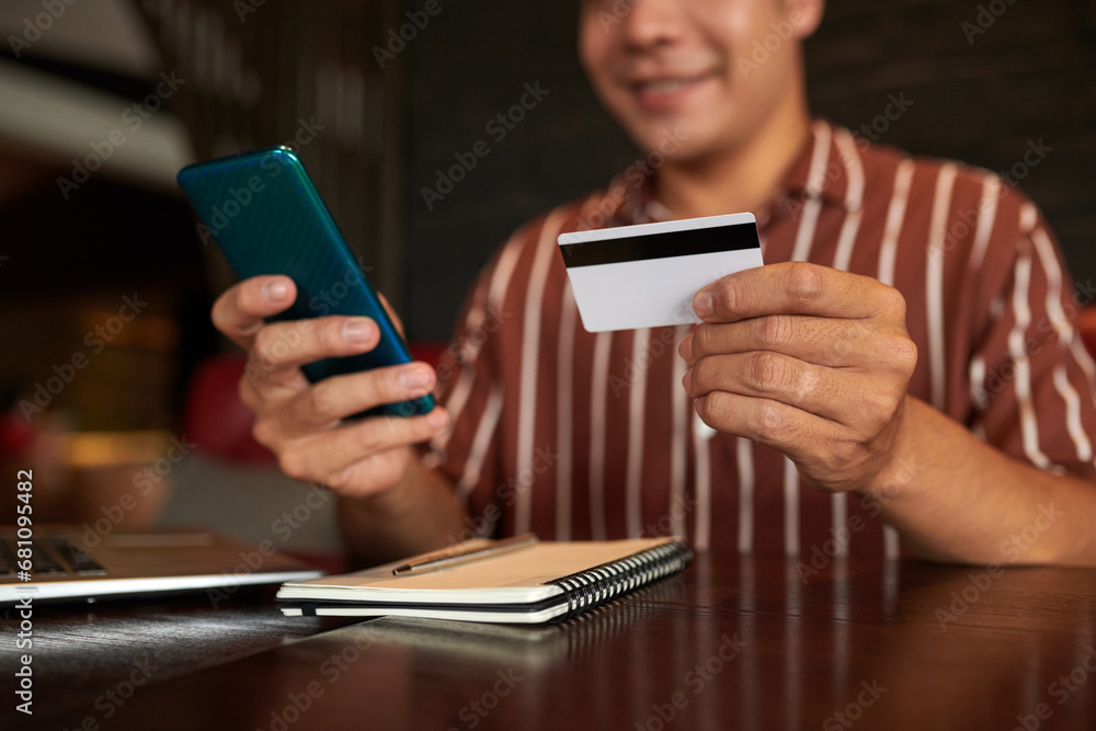 Cropped image of smiling man paying with credit card when shopping in mobile application Cropped image of smiling man paying with credit card when shopping in mobile application