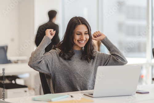 Overjoyed Indian woman using laptop computer celebration success sitting in modern office photo