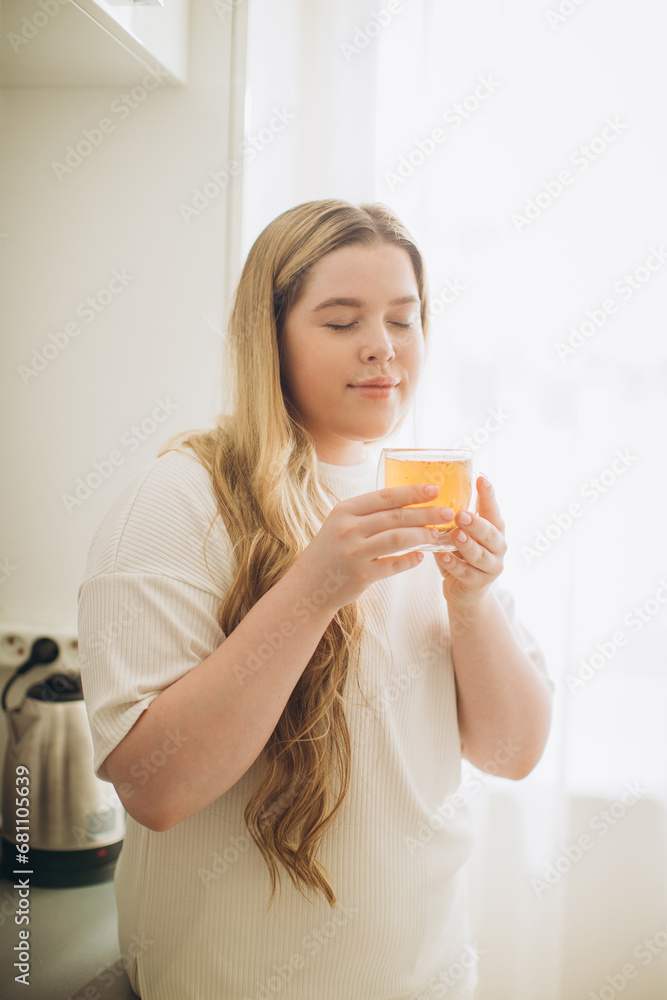 Portrait of smiling young woman holding cup of hot tea in hands in the morning in a kitchen Portrait of smiling young woman holding cup of hot tea in hands in the morning in a kitchen