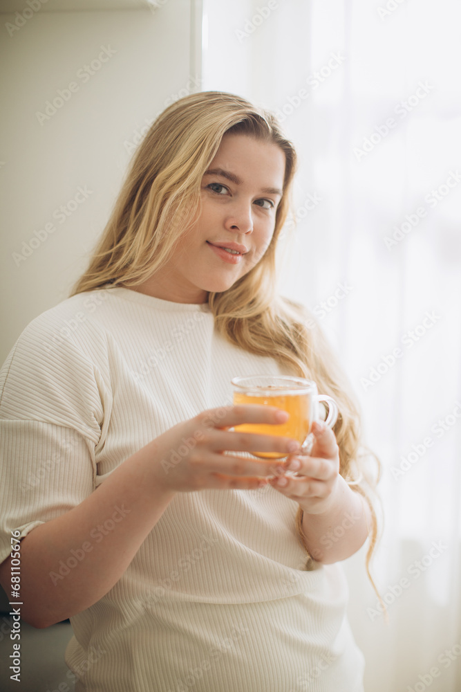 Portrait of smiling young woman holding cup of hot tea in hands in the morning in a kitchen Portrait of smiling young woman holding cup of hot tea in hands in the morning in a kitchen