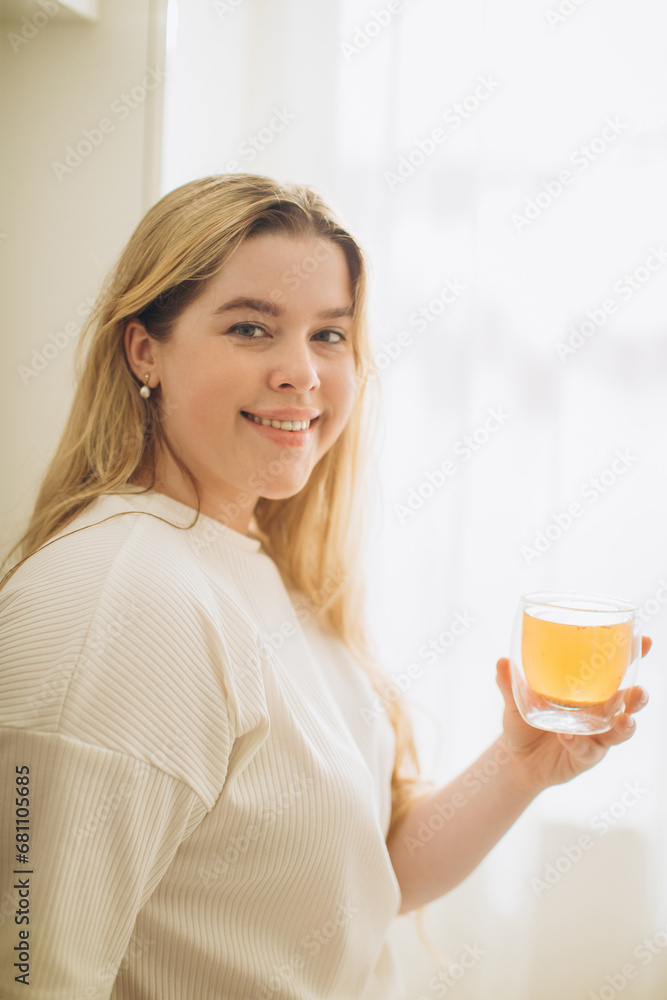 Portrait of smiling young woman holding cup of hot tea in hands in the morning in a kitchen Portrait of smiling young woman holding cup of hot tea in hands in the morning in a kitchen