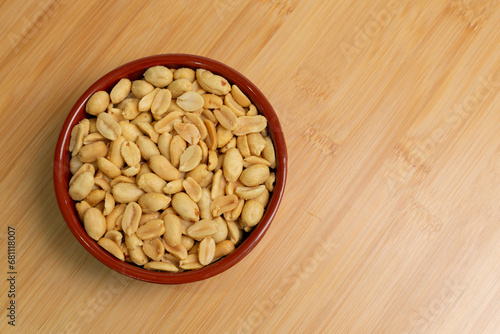 Top view of peanuts in bowl on wooden patterned background. Free text space with wooden pattern. Roasted, peeled, salted peanuts close-up.
