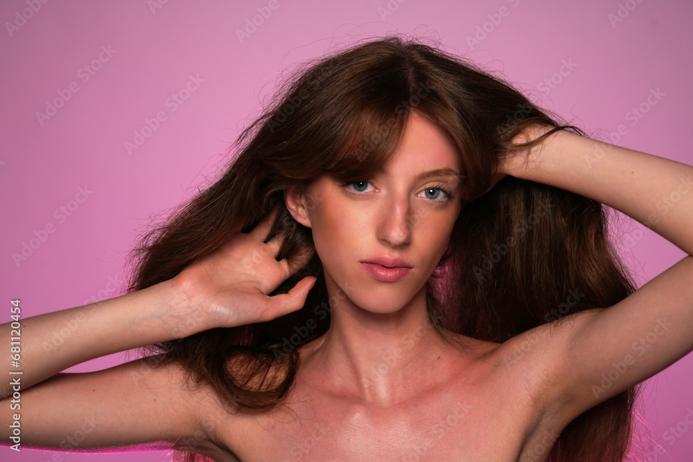 Long haired woman enjoying the softness and silkiness of her hair while touching it. Seminude woman in studio on pink background in pink neon light close up. Concept of beauty, hair care, treatment. Long haired woman enjoying the softness and silkiness of her hair while touching it. Seminude woman in studio on pink background in pink neon light close up. Concept of beauty, hair care, treatment.