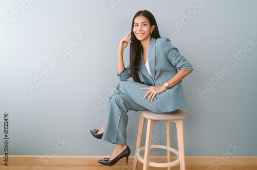 Portrait of beautiful Asian business woman sitting on chair and looking away posing on green pastel background, Full length photo.