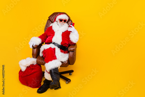 Full body photo of funny saint nicholas grandfather browsing smartphone searching eshopping xmas offers isolated on yellow color background © deagreez