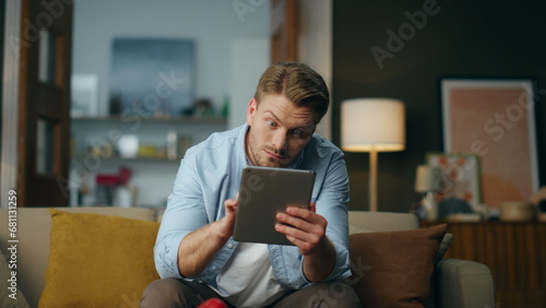 Surprised businessman looking pad screen sitting sofa. Wondering guy reading tab