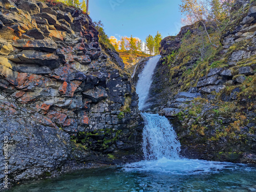 A beautiful waterfall in the autumn mountains beyond the Arctic Circle in the north, in Khibiny, Murmansk region. Panoramic view of a beautiful waterfall in the mountains in autumn, Kola Peninsula