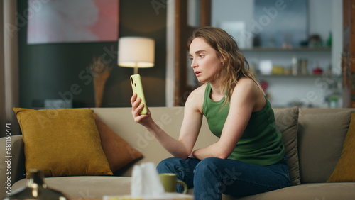 Unhappy woman looking telephone screen at living room. Sad girl getting bad news