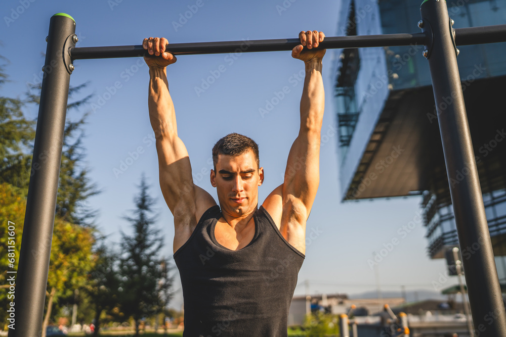 One man muscular male athlete training pull ups outdoor in sunny day One man muscular male athlete training pull ups outdoor in sunny day