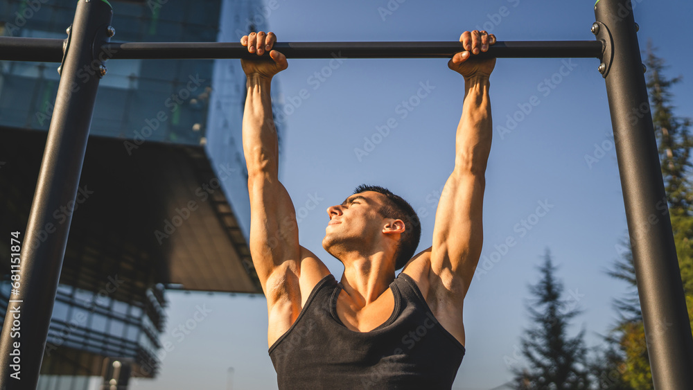 Naklejka premium One man muscular male athlete training pull ups outdoor in sunny day
