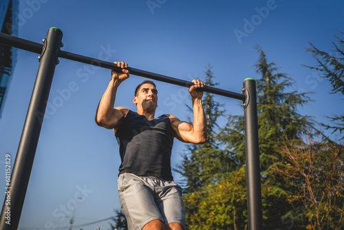 One man muscular male athlete training pull ups outdoor in sunny day
