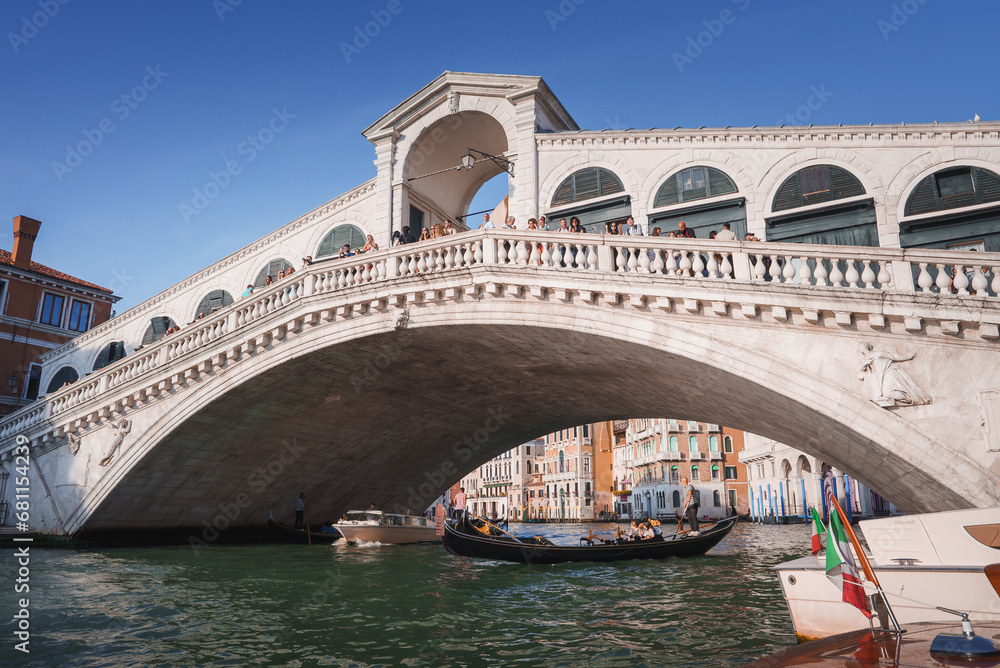The iconic Rialto Bridge in Venice, Italy, spans the Grand Canal, a famous landmark in a bustling area with many other attractions nearby.