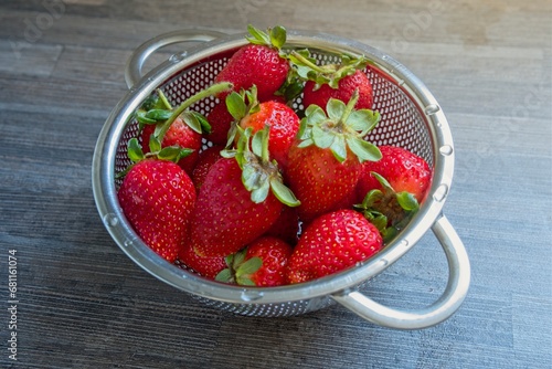 Ripe strawberries in a small stainless steel colander on kitchen counter
