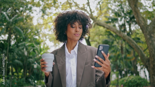 Woman talking phone video call walking city park hold paper coffee cup closeup.