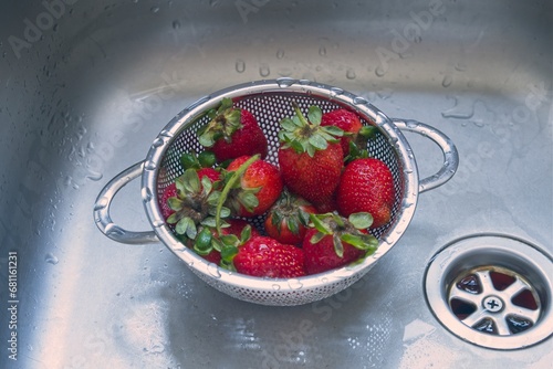 Ripe strawberries in a small stainless steel colander in a kitchen sink