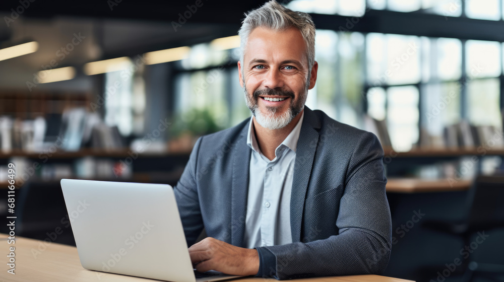 Mature, smiling businessman with a gray beard, working on a laptop at a table