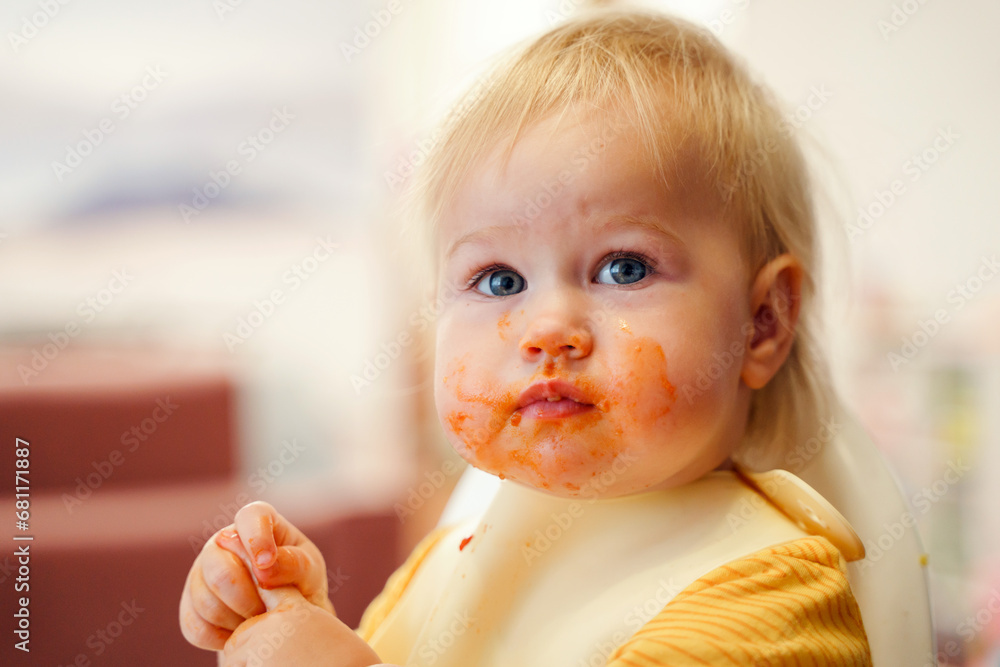 Cute toddler little child eats in a bib on a high chair, mouth dirty in sauce Cute toddler little child eats in a bib on a high chair, mouth dirty in sauce