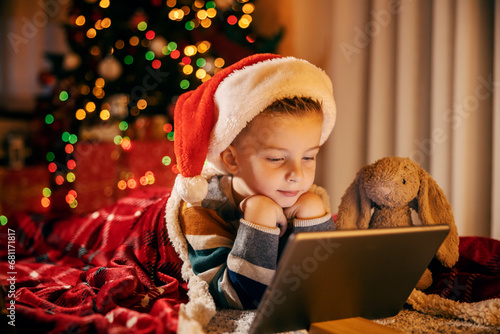 Canvas Print A cute boy is looking at tablet with his bunny toy friend at christmas and new year's eve