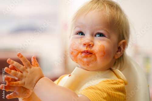 Cute toddler little child eats in a bib on a high chair, mouth dirty in sauce photo