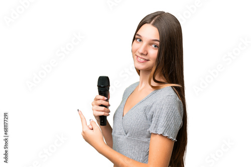 Teenager singer girl picking up a microphone over isolated background pointing back