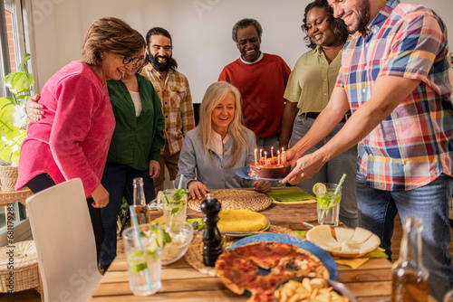 group of multiracial family and friends celebrating birthday at home with a cake with candles.