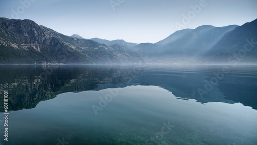 High mountains reflecting in calm sea waves with rising morning fog or mist