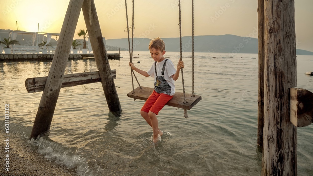 Little boy enjoying riding on swing at the sea beach. Holiday, summer vacation and tourism