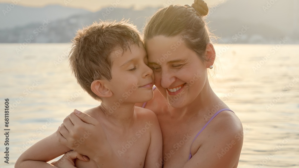 Portrait of loving mother and son hugging each other while relaxing on the sea against sunset light rays Portrait of loving mother and son hugging each other while relaxing on the sea against sunset light rays