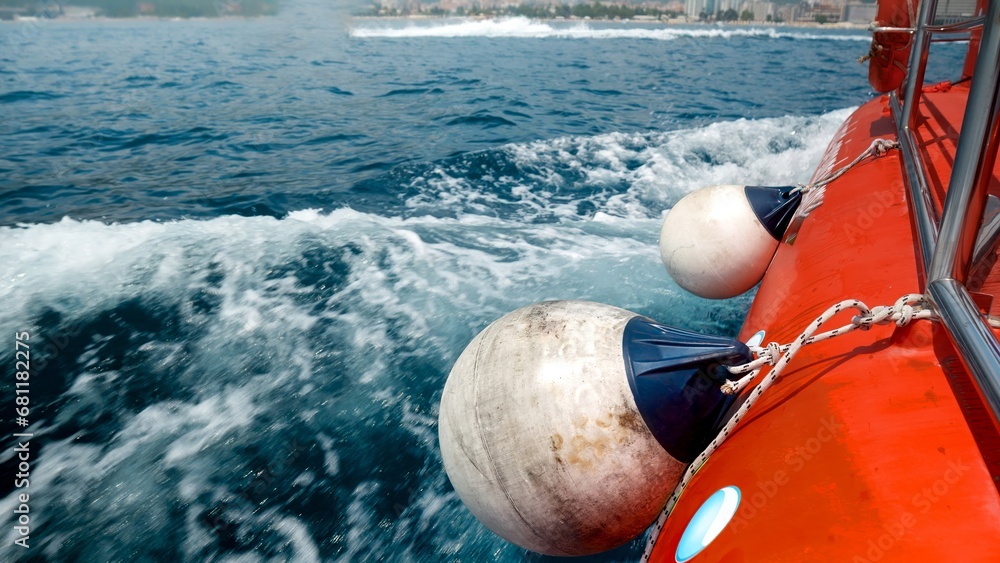 Fototapeta premium Closeup of fenders, ropes and buoys hanging on the side of red boat sailing in sea bay