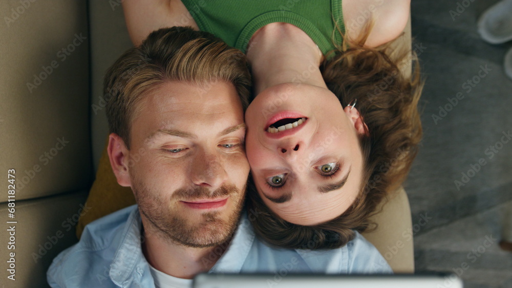 Fototapeta premium Love couple taking selfie laying sofa top view. Loving pair trying face mask app