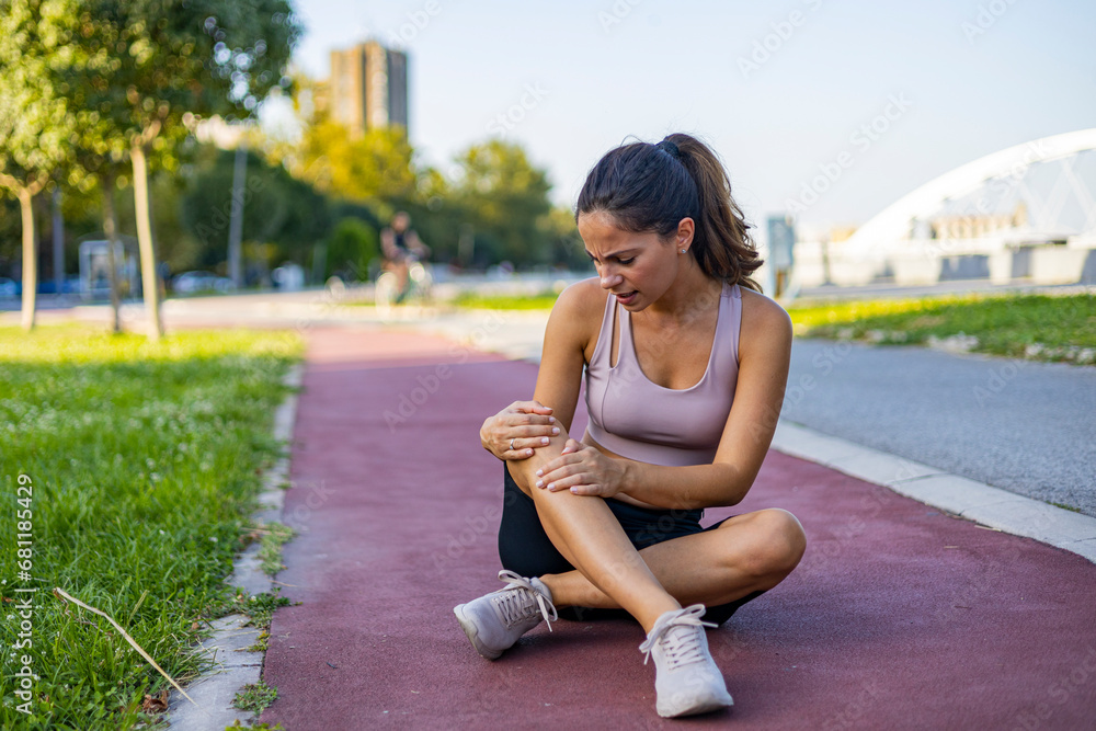 Young sportswoman having pain / injury during exercise and jogging in the park. Young woman taking a break from running, having a knee injury.
