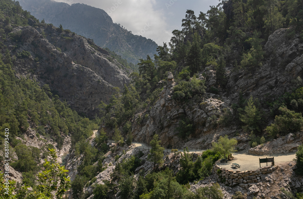 Panoramic view of the Goynyuk Canyon. A small mountain stream runs through a wide rocky gorge. The steep slopes are covered with Mediterranean forest. A recreation area area by the road.