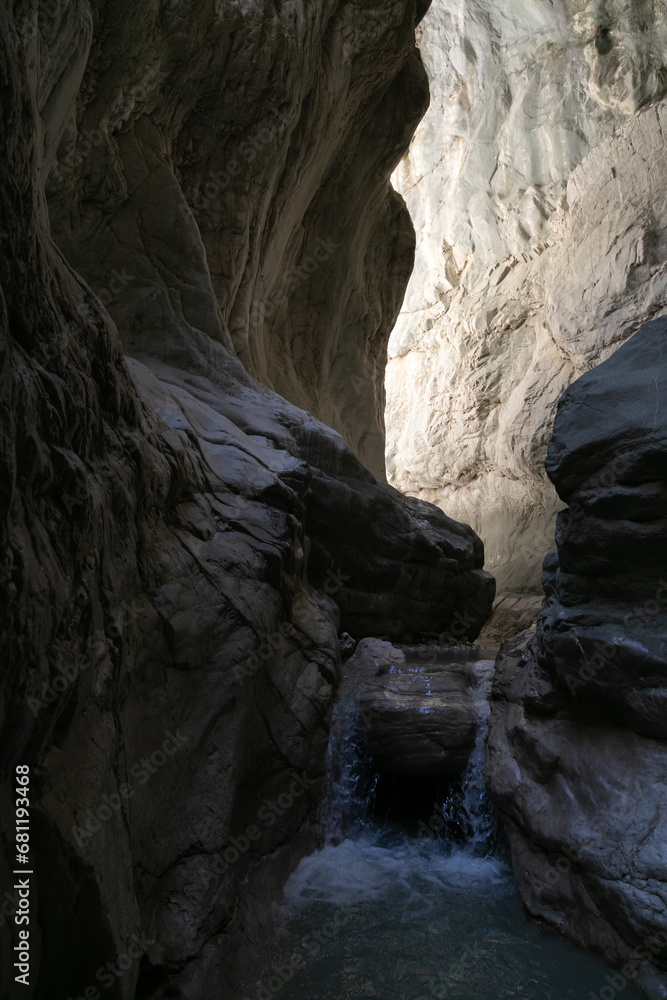 A narrow passage among steep cliffs in a mountain gorge. A swift mountain stream flows at the bottom of the gorge. Fascinating trekking in the mountain park of Saklikent Canyon.