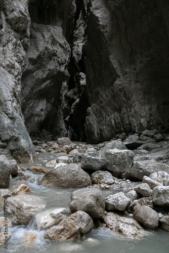A narrow passage among steep cliffs in a mountain gorge. A swift mountain stream flows at the bottom of the gorge. Fascinating trekking in the mountain park of Saklikent Canyon.