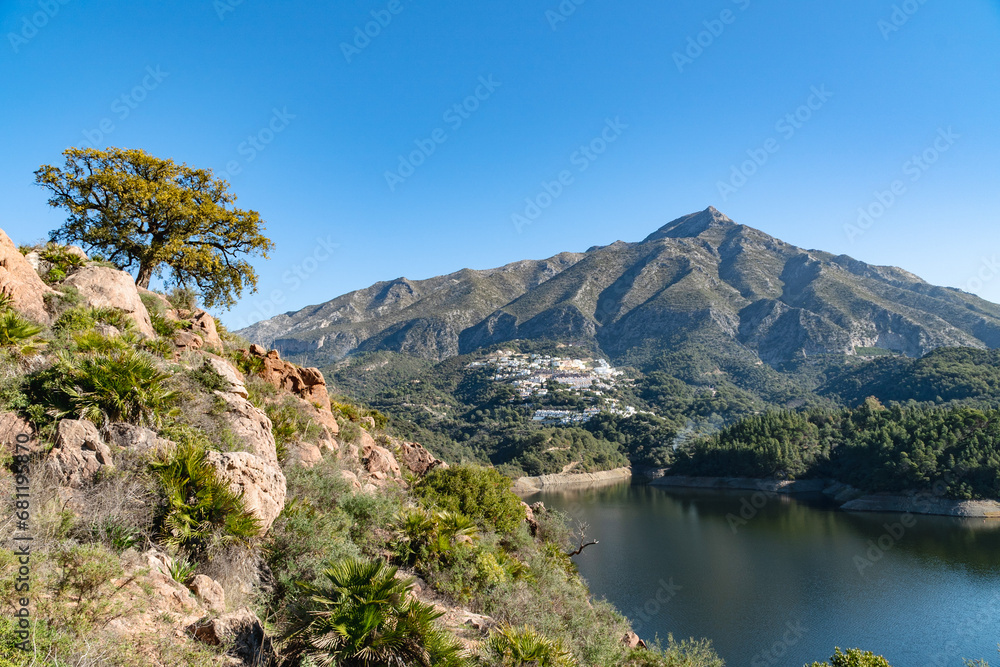 a view from a cliffside overlooking a reservoir and pueblo Blanco at the foot of a mountain along the Costa Del Sol. 