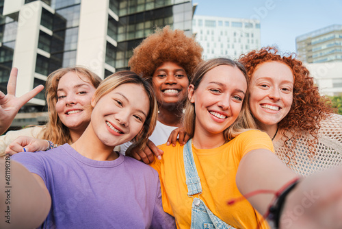 Group of young feminine women taking a selfie portrait  smiling looking at camera. Teenage girls laughing and posing for the social media photo. Multiracial excited females having fun staring front