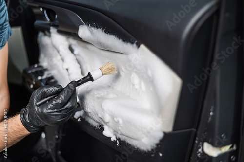 A man cleans the interior of a car with foam and a brush. Clean the door trim.